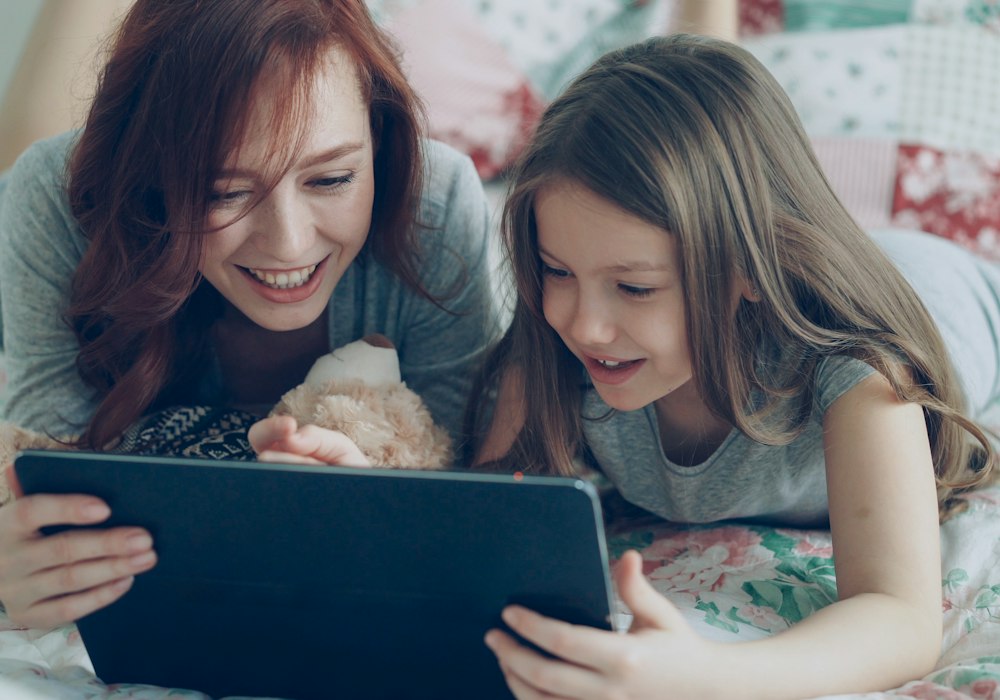 A parent and child smiling at a tablet